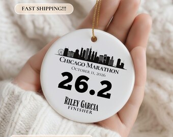 May include: A round white ceramic ornament featuring a black silhouette of the Chicago skyline, the text CHICAGO MARATHON, OCTOBER 11, 2026, the number 26.2, and the name RILEY GARCIA FINISHER. The ornament hangs from a thin gold string.