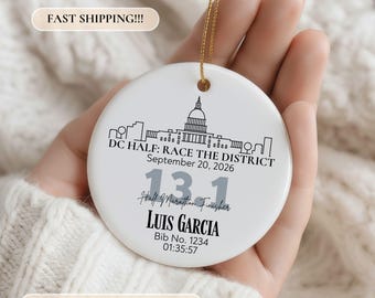 May include: A round white ceramic ornament featuring a black line drawing of the Washington DC skyline, the text DC HALF: RACE THE DISTRICT, September 20, 2026, 13.1, Half Marathon Finisher, LUIS GARCIA, Bib No. 1234, and the time 01:35:57.