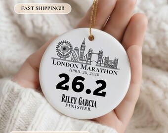 May include: A round white ceramic ornament featuring a black line art illustration of the London skyline, the text LONDON MARATHON APRIL 26, 2026, the number 26.2, and the name RILEY GARCIA FINISHER, suspended by a thin gold string for hanging.