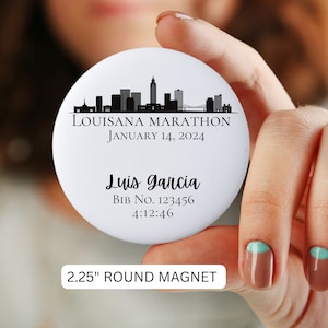 May include: A 2.25 inch round magnet featuring a black and white silhouette of a city skyline. The text "LOUISANA MARATHON JANUARY 14, 2024" is printed above the skyline. Below the skyline, the text "Luis Garcia BIB NO. 123456 4:12:46" is printed.