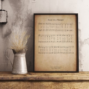 Puede incluir: Una impresión de estilo vintage con la letra y la partitura de la canción navideña "Away in a Manger". La letra está impresa en tinta negra sobre un fondo crema con un aspecto desgastado. El título "Away in a Manger" está impreso en negro en la parte superior de la página.