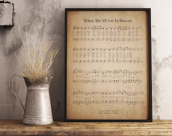 May include: A framed print of sheet music titled "When We All Get To Heaven." The print has a vintage, aged appearance with musical notes and lyrics. A metal pitcher with dried wheat stands to the left, adding a rustic touch.