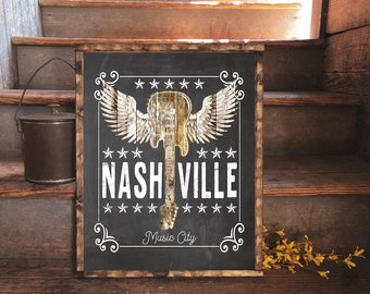 May include: Black chalkboard sign with white text and a white silhouette of a guitar with wings. The text reads "Nashville Music City".