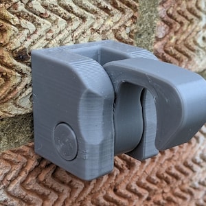 May include: A grey plastic wall mount with a hook. The hook is designed to hold a small object, such as a bag or a towel.