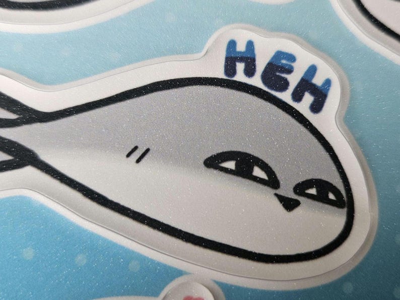 Peut inclure: Un poisson de dessin anim&eacute; blanc et gris avec des contours noirs et une texture scintillante. Le poisson a la bouche ferm&eacute;e et deux yeux. Le poisson dit "HEH" en lettres bleues et noires.