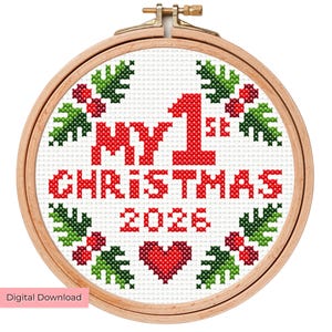 Puede incluir: Un bastidor de bordado circular de madera que contiene un patrón de punto de cruz sobre tela blanca. El diseño presenta el texto rojo MY 1ST CHRISTMAS 2026, un corazón rojo y un borde de hojas de acebo verdes con bayas rojas sobre fondo blanco.