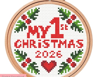 May include: A circular wooden embroidery hoop containing a cross-stitch pattern on white fabric. The design features red text reading MY 1ST CHRISTMAS 2026, a red heart, and a border of green holly leaves with red berries on a white background.