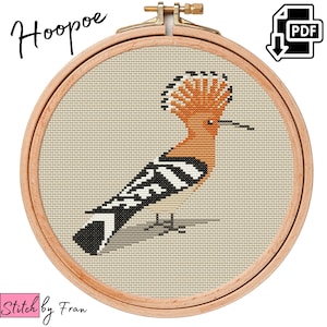 Puede incluir: Patrón de punto de cruz de un abubilla con un pico largo y una cresta de plumas distintiva. El pájaro está representado en tonos de naranja, negro y blanco sobre un fondo beige. El patrón está enmarcado en un aro de bordado de madera.