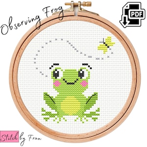 May include: A cross stitch pattern of a green frog with a yellow belly and pink cheeks, observing a yellow butterfly flying away. The pattern is in a wooden embroidery hoop. The text "Observing Frog" is written above the hoop.