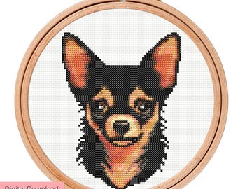 以下が含まれることがあります： 丸い木製の刺繍枠の中央に配置された犬の頭のクロスステッチパターン。犬は黒い毛並みで、耳、鼻先、胸元にオレンジとタンのハイライトがあり、白い布の背景に刺繍されています。