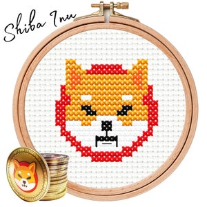 May include: A cross-stitch embroidery hoop with a pixelated Shiba Inu dog design. The dog is red, yellow, and white. The hoop is made of wood and has a natural finish.