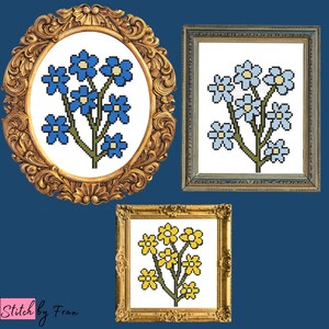 Op de afbeelding: Drie ingelijste kruissteekborduurwerken met bloemboeketten. Het eerste ontwerp heeft blauwe bloemen met gele centra, het tweede heeft lichtblauwe bloemen met witte centra en het derde heeft gele bloemen met blauwe centra.