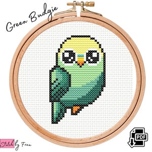 May include: Cross stitch pattern of a green budgie with yellow head and black eyes. The pattern is in a wooden embroidery hoop. The text "Green Budgie" is above the hoop. The text "Stitch by Fran" is below the hoop. A PDF download icon is in the lower right corner.