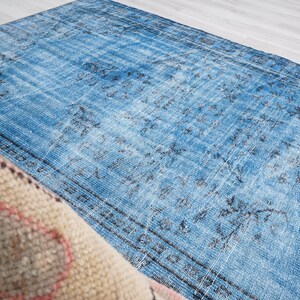 May include: A vintage blue rug with a faded floral pattern. The rug has a distressed look and is made of a soft, woven material.