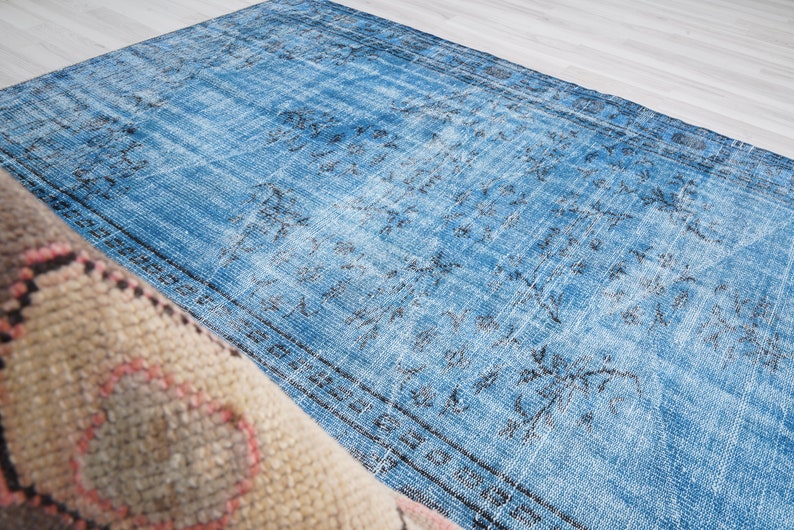 May include: A vintage blue rug with a faded floral pattern. The rug has a distressed look and is made of a soft, woven material.