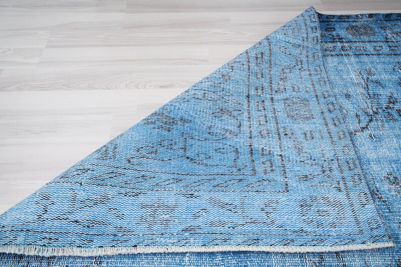 May include: A blue and black patterned rug with a fringed edge. The rug is folded in half and the pattern is visible on both sides.