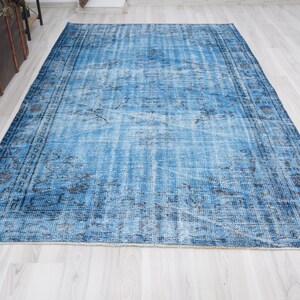 May include: A vintage blue rug with a faded floral pattern and a dark blue border. The rug has a distressed look and is made of a soft, woven material.