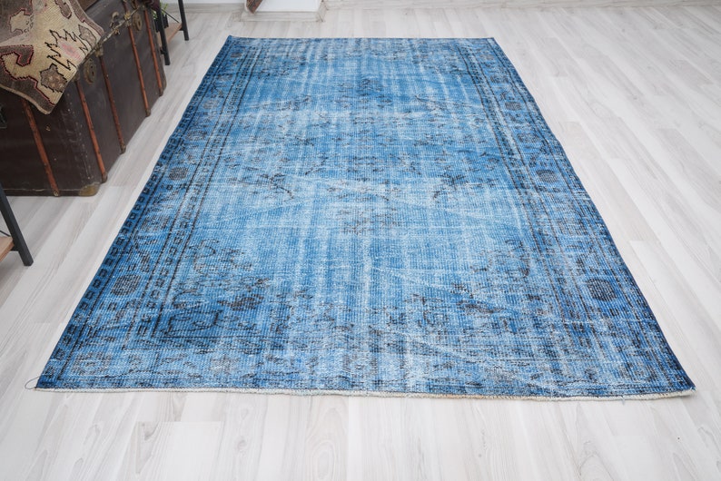 May include: A vintage blue rug with a faded floral pattern and a dark blue border. The rug has a distressed look and is made of a soft, woven material.