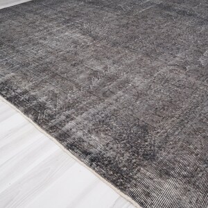 May include: A dark gray rug with a distressed, vintage look. The rug has a subtle pattern throughout and a slightly frayed edge.