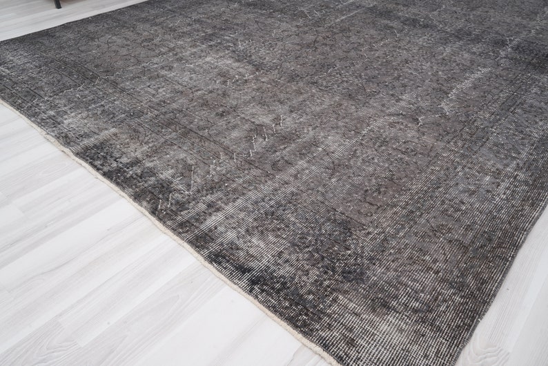 May include: A dark gray rug with a distressed, vintage look. The rug has a subtle pattern throughout and a slightly frayed edge.