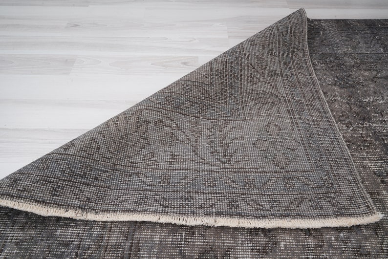 May include: A close-up of a gray and brown patterned rug with a fringed edge. The rug is folded in half, revealing the underside.