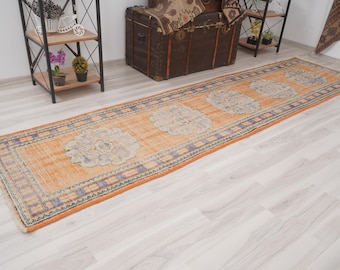 Op de afbeelding: Een oranje en blauw loper met een bloemenpatroon. Het tapijt heeft een rechthoekige vorm en ligt op een lichtgekleurde houten vloer. Het ontwerp toont herhaalde bloemenmedaillons.