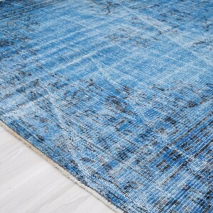 May include: A blue and black distressed rug with a faded floral pattern. The rug has a soft, worn texture and a fringed edge.