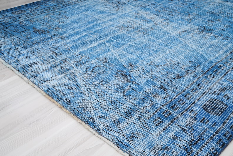 May include: A blue and black distressed rug with a faded floral pattern. The rug has a soft, worn texture and a fringed edge.