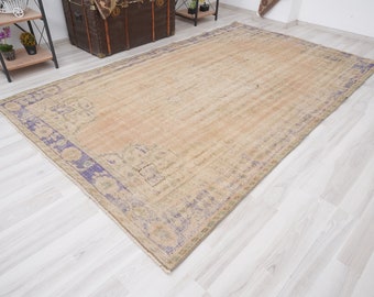 May include: A vintage rug with a light beige background and a faded purple border. The rug has a distressed look and a subtle pattern.