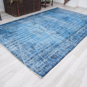 May include: A vintage blue and white rug with a faded floral pattern. The rug has a distressed look and is made of a soft, woven material.