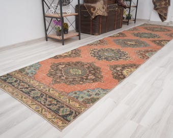 May include: A vintage runner rug with a faded orange background and intricate floral patterns in shades of brown, blue, and green. The rug has a border with a repeating pattern.