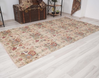 May include: A rectangular beige rug with a floral pattern in shades of red, pink, and blue. The rug is placed on a light-colored wooden floor. A brown trunk and shelves are visible in the background.