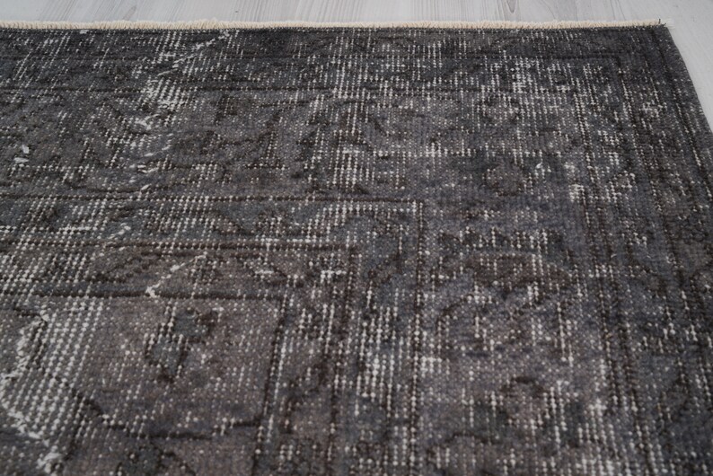 May include: A dark gray rug with a subtle pattern of white and gray. The rug has a distressed look and a slightly textured surface.