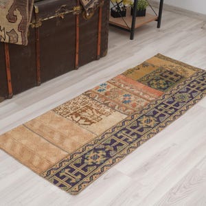May include: A rectangular, patchwork rug with a variety of patterns and colours. The rug features a beige base with sections of orange, blue, and brown. A dark blue border with geometric designs frames the rug. The rug is placed on a light wood floor.