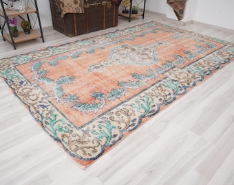 May include: A vintage rug with a peach background and a floral pattern in shades of blue, green, and cream. The rug has a faded, distressed look, giving it a unique and charming character.