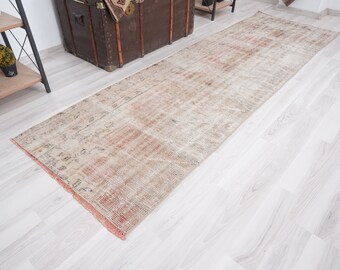 May include: A vintage-style runner rug with a faded, distressed look. The rug has a light beige background with a subtle pattern in shades of brown and pink.