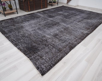 May include: A dark gray distressed rug with a subtle pattern. The rug has a white border and is laid out on a light wood floor.
