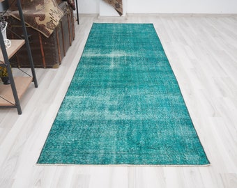 May include: A teal blue vintage distressed rug with a faded, worn look. The rug has a rectangular shape and is laid out on a white wooden floor.