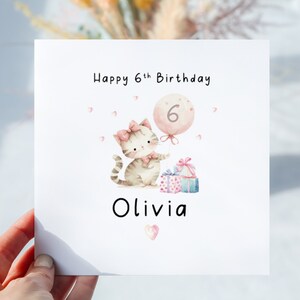 May include: A white birthday card with a watercolor illustration of a kitten holding a balloon with the number 6. The card reads "Happy 6th Birthday Olivia" with pink accents and gift boxes.