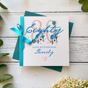 80er Geburtstagskarte für Sie. Hübsche handgemachte personalisierte Geburtstagskarte. Türkis und Weiß mit Schleife, Gems und Papierblumen.