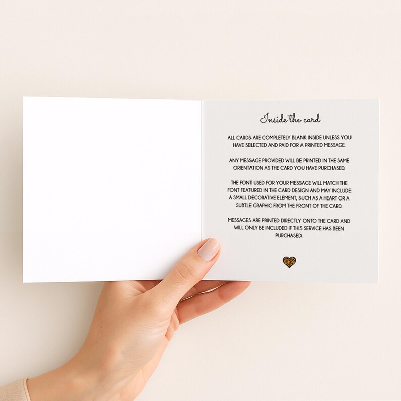 May include: An open, white greeting card held by a person's hand, revealing the inside. Text on the right side reads "Inside the card" followed by details about printed messages and design elements. A small gold heart graphic is at the bottom.