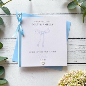 Nouvelle carte pour bébé garçon, joli noeud, prénoms personnalisés des parents, nom du bébé et date de naissance. Un nœud et une fleur sont finis à la main