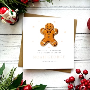 May include: A festive Christmas card featuring a gingerbread man. The card includes the message "Happy First Christmas to a Special Grandson", the name "Noah George", and the year "Christmas 2025". It rests on a brown envelope.