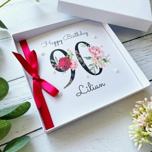 90e anniversaire dans une boîte | Personnalisé | Grands chiffres avec des fleurs | Ruban et noeud | Rouge | Prénom féminin | Joyeux anniversaire | Perles