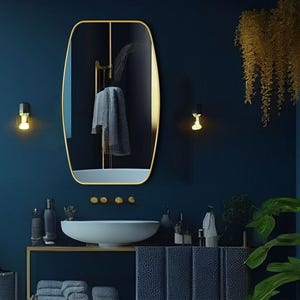 May include: A gold-framed oval mirror hangs above a white porcelain sink in a bathroom with dark blue walls. Two wall sconces with light bulbs illuminate the mirror. A towel hangs on a rack in the mirror's reflection.