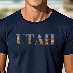 May include: A navy blue t-shirt with the word "UTAH" printed in white. The letters are filled with a landscape image of red rock formations.