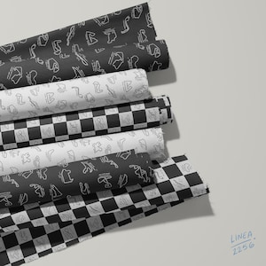 Puede incluir: Seis rollos de tela con varios patrones en blanco y negro, incluyendo diseños de cuadros y contornos de circuitos de carreras. Los rollos de tela están dispuestos en una pila, mostrando una mezcla de motivos negros, blancos y a cuadros.
