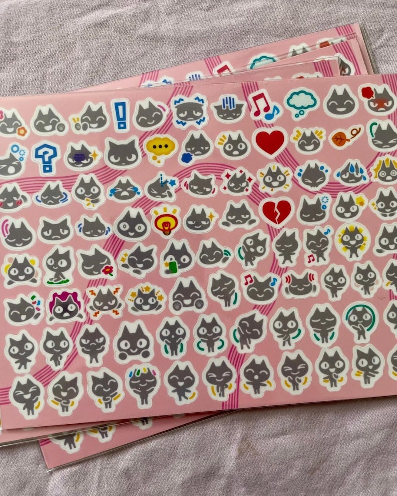 May include: A sheet of stickers featuring black cats with different expressions and actions. The stickers are on a pink background with black and white stripes.