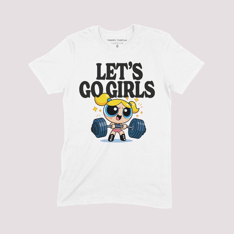 K&ouml;nnte beinhalten: Wei&szlig;es T-Shirt mit einer Cartoon-Illustration einer Figur, die Gewichte hebt, und dem Text "LET'S GO GIRLS". Das Design zeigt eine blonde Figur mit blauen Augen und eine Langhantel mit blauen Gewichten. Das Shirt hat einen Rundhalsausschnitt.