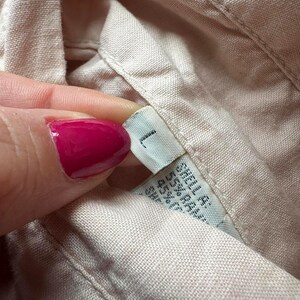 May include: A close-up of a beige fabric shirt with a white tag that says "1" and has additional text in a smaller font.